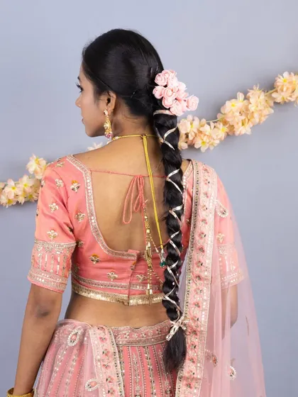 The back view of the peach lehenga, showcasing an intricately braided hairstyle decorated with flowers, which perfectly complements the outfit.