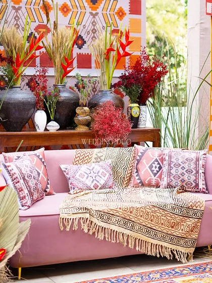 A close-up of our African tribal-inspired decor. The pink sofa is layered with printed cushions and a block-print throw, surrounded by rustic pottery and bold red and orange florals.