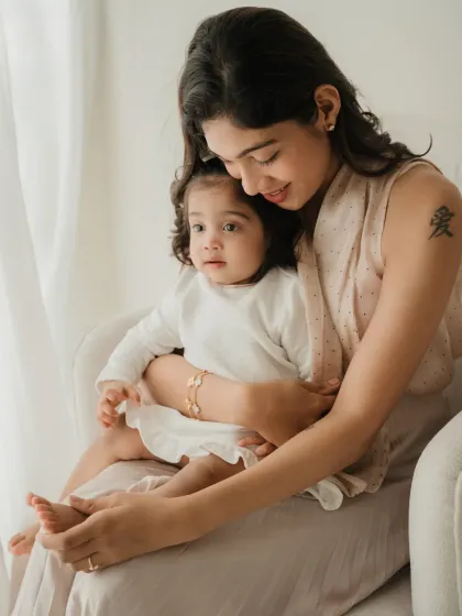 A mother sits with one of her twin daughters, sharing a quiet, tender moment. The tattoo on her arm, which means 'love', adds a personal touch.