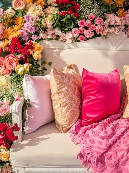 A close-up of the lush floral arrangement on the Mehendi seating, showing a mix of roses in shades of pink, orange, and red. The vibrant colors are perfect for a sunny Goan celebration.