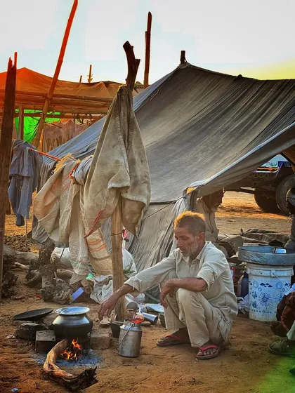 A man cooking over an open fire at his makeshift tent. This photo documents the rustic and authentic living conditions of the traders during the fair.