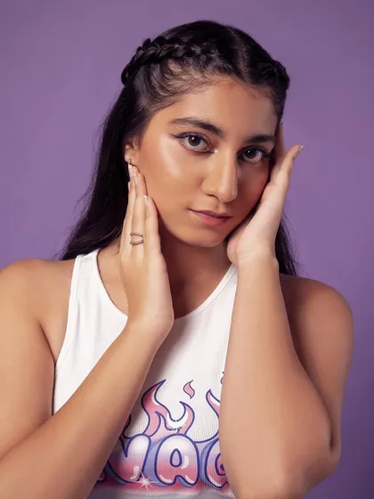 A fun and youthful portrait against a vibrant purple background. The winged eyeliner and braided hair complete the trendy look.