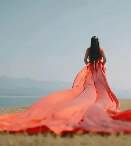 The sheer scale of this coral gown's trail creates a breathtaking landscape shot. It's perfect for capturing a sense of grandeur and romance in a pre-wedding shoot.