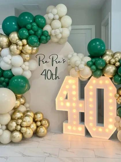 A 40th birthday celebration with a large "40" marquee number and a balloon arch in emerald green, gold, and cream.