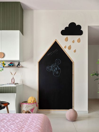 This kids' room features a whimsical house-shaped chalkboard, perfect for unleashing creativity. The study area combines olive green and white cabinets with circular wooden knobs for a playful yet stylish look.