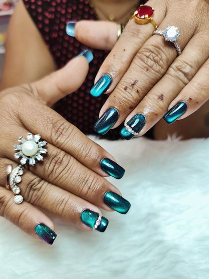 I can’t take my eyes off these cat-eye nails. This set features a stunning teal and black ombré cat-eye effect, accented with a row of crystals for extra glam.