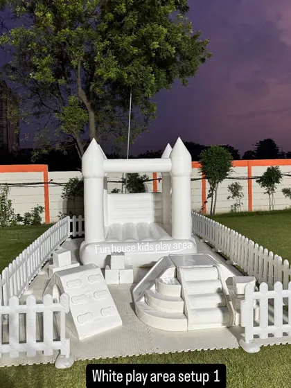 A complete white play area setup perfect for toddlers, featuring a small bounce house, soft climbers, and steps, all safely enclosed by a white picket fence.
