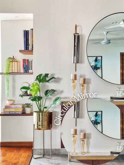 A large circular mirror makes a bold statement in this space. Paired with a brass planter and decorative wall sconces, it enhances light and adds a sense of glamour and depth.