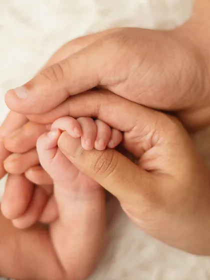 An intimate close-up shot of a newborn's tiny foot being gently cradled by their parents' hands on a soft, white, fluffy surface. This image captures the delicate details of a new life.