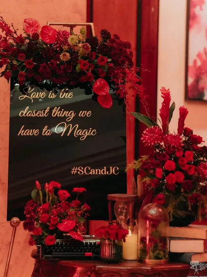 A welcome sign for the vintage-themed sangeet, surrounded by deep red flowers and antique books.