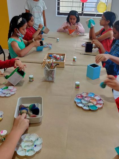 A wide shot of a birthday party where kids are busy painting pen stands and other fun projects.