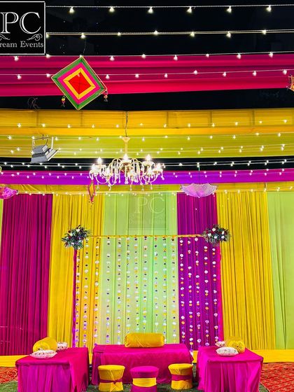 The main seating area for the Mehndi function, featuring a backdrop of yellow, green, and pink drapes with traditional mirror work hangings.