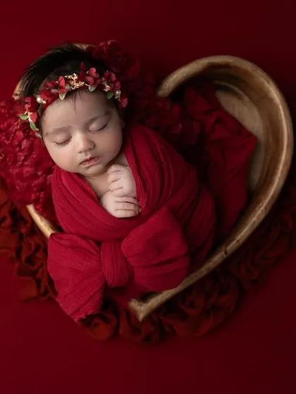 All you need is love. This newborn girl is wrapped in a rich red swaddle and placed in a heart shaped wooden bowl, creating a bold and beautiful statement portrait.
