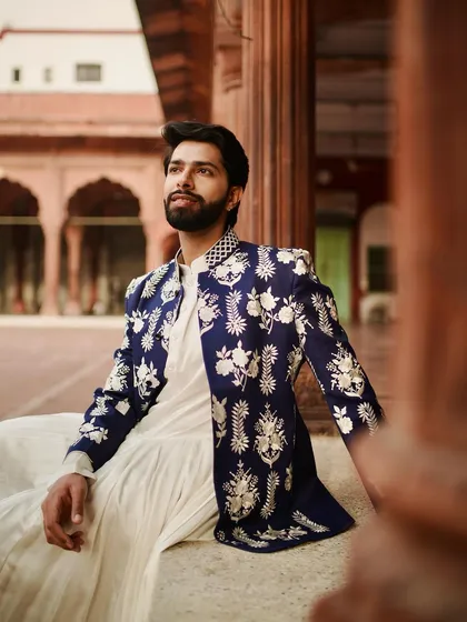 Here, tradition meets a modern aesthetic. A crisp white pleated kurta is layered with a navy blue Nehru jacket, featuring stunning silver floral embroidery that feels both classic and contemporary, perfect for a man with discerning taste.