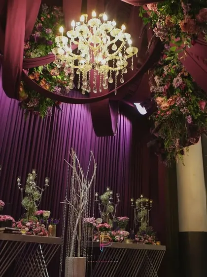 We believe in decorating from top to bottom. Here, the ceiling is adorned with draped fabric and a floral-wrapped chandelier, adding to the immersive and opulent feel of the event.