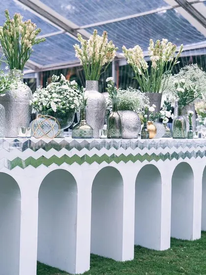 A bar station decorated with an array of white flowers in silver and glass vases. Even functional areas are designed to be beautiful and cohesive with the overall theme.