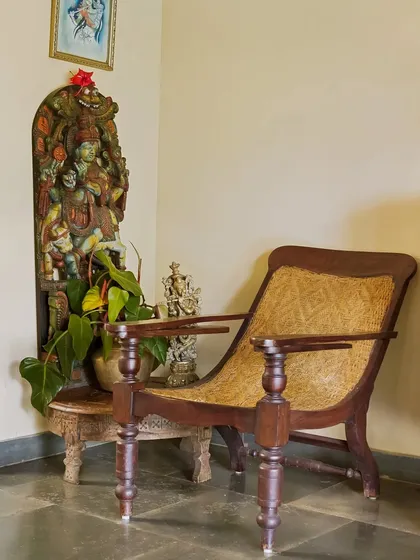 A classic planter's chair in a corner of Villa Magnolia, Coorg, next to a traditional Hindu sculpture. This vignette beautifully represents the blend of colonial history and local culture.