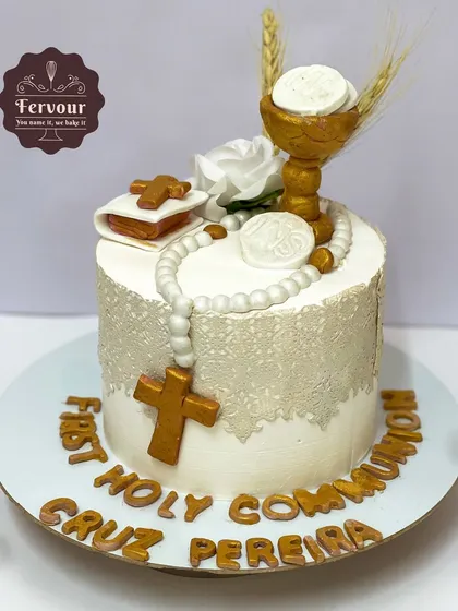 A First Holy Communion cake designed with religious symbols like a cross, rosary, and bible, all handcrafted from fondant. The cake is finished with an edible lace wrap for a delicate and reverent look.