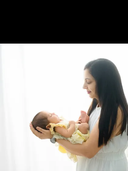 A mother holds her sleeping baby, who is dressed in a sunny yellow outfit. The soft, bright light creates an angelic and peaceful mood.