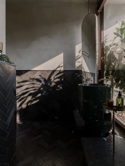 Even a powder room can be a sanctuary. We used dramatic shadows, dark herringbone tiles, and a custom-carved green marble sink to transform this small space into a memorable experience, proving that luxury hospitality design extends to every corner.