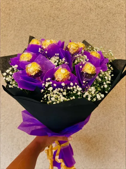 A striking bouquet featuring Ferrero Rocher chocolates wrapped in a rich purple, contrasted against black paper and accented with baby's breath. This arrangement is designed to make a bold and elegant statement.