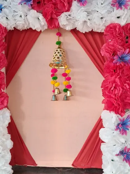 This backdrop features a simple diamond-shaped drape in the center, highlighted by a large hanging bell. The frame is made of white and bright pink artificial flowers, creating a bold contrast.