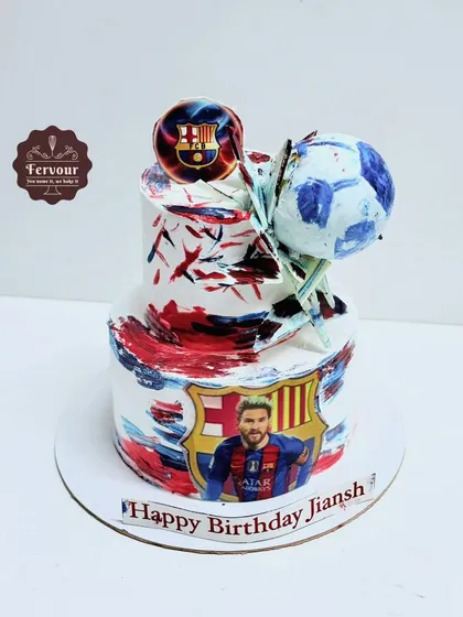 A football theme cake for a Lionel Messi fan. This two-tier cake has an abstract paint design and is decorated with the Barcelona logo and a picture of the football star.