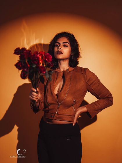 A dramatic portrait using a single spotlight. The contrast between the warm light, the dark shadows, and the red roses creates a powerful and theatrical image.