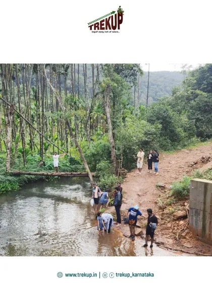 Trekkers enjoying a break by a stream, with some crossing a makeshift bamboo bridge.