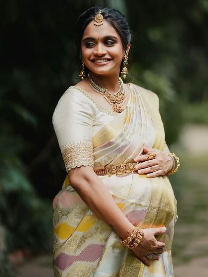 A beautiful maternity portrait. The client cradles her baby bump, wearing the elegant off-white saree and custom blouse with scalloped sleeve details.