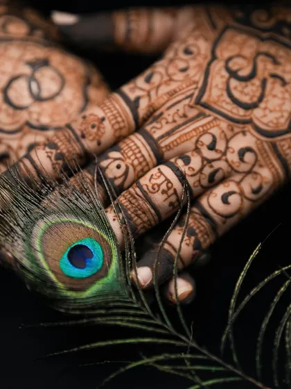 A close-up shot of the engagement mehndi, with a peacock feather drawing attention to the fine details and the "Shubh" (auspicious) text.