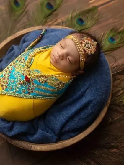 A wider view of the Janmashtami setup, with the baby nestled in a wooden bowl surrounded by beautiful peacock feathers.