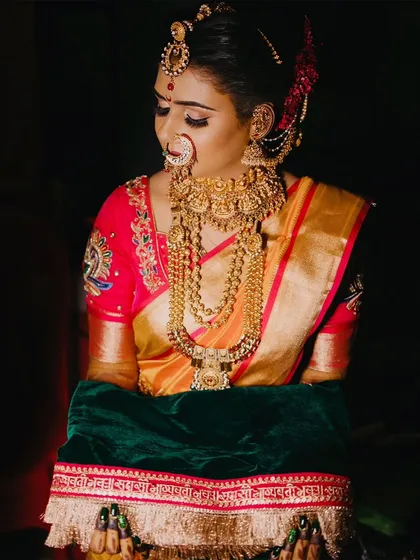 A low-light portrait of a bride holding her 'shetkari' shawl, highlighting the rich colors and gold jewelry.