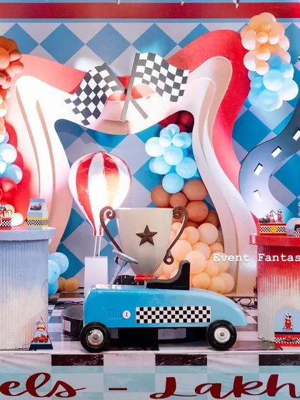 A vibrant and playful racing theme setup. This backdrop features wavy road elements, a trophy, a cute blue race car, and colorful balloon garlands.