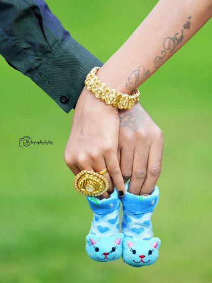 A close-up shot of a couple's hands holding tiny blue baby socks, a sweet detail from a traditional maternity shoot.
