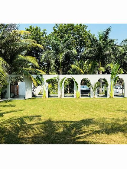 A wide view of the "Tropical Manor" lawn, where the arched wall acts as a sculptural backdrop to a sprawling green oasis, separating the garden from the driveway.