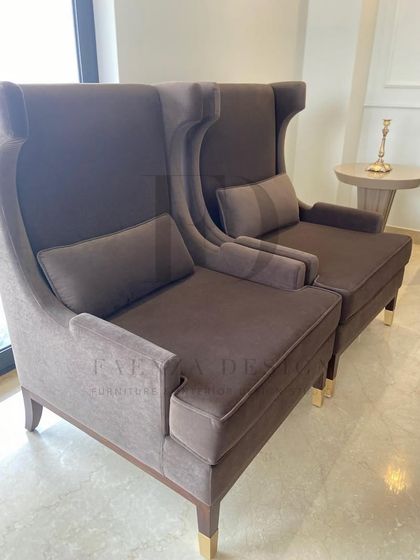 A pair of elegant, high-back lounge chairs in a deep brown fabric. Paired with a sleek, modern side table, they create a sophisticated and comfortable seating area by the window.