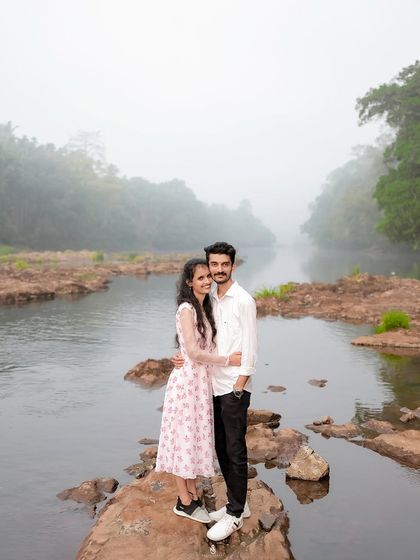 A beautiful wide shot of the couple standing on rocks in the middle of the river, showcasing the scale and beauty of the natural landscape.