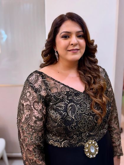 A classic party look featuring soft, voluminous curls and natural-looking makeup that enhances the client's features. The black lace dress is complemented by a subtle glow and a gentle smile.