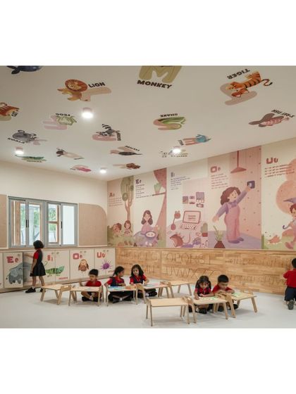 An active classroom scene where children are learning and creating. The walls and even the ceiling are used for educational graphics, like the alphabet paired with animals, making learning a constant, passive experience.