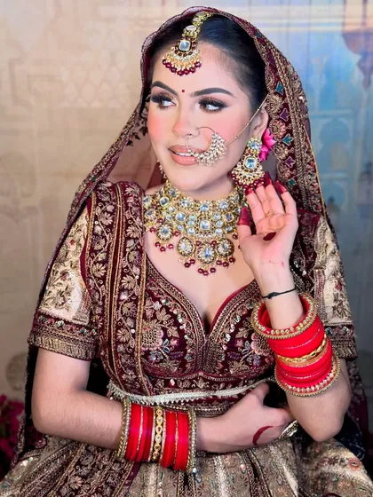 A close-up of a gorgeous bride in a maroon velvet lehenga. The makeup features a soft smokey eye with a hint of gold glitter, perfectly complementing her outfit.