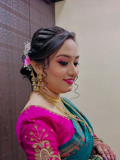 A side view of a soft, romantic updo with loose curls framing the face and pink flowers tucked into the bun.