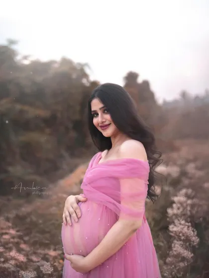 A beautiful outdoor portrait in a pink tulle gown. The soft, misty background of the field creates a dreamy and romantic atmosphere, perfect for an ethereal maternity shoot.