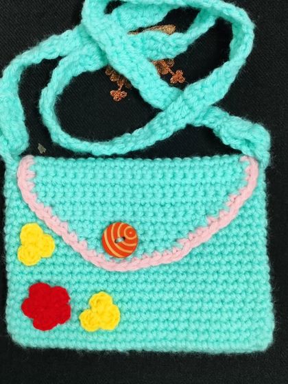 This is a cute little handmade bag for kids. I made it with turquoise yarn and decorated it with small flowers. It has a simple flap and a colourful button.