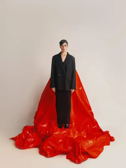 A minimalist, full-length portrait that uses the red fabric to create a sense of scale and drama. The model's simple, strong stance makes a powerful statement.