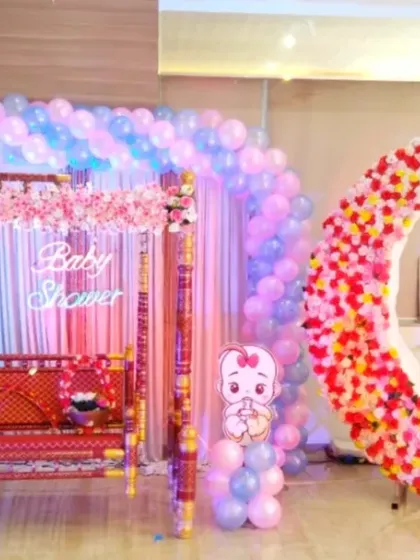 For this 'Dohale Jevan' baby shower, I combined modern and traditional elements. The setup features a large pastel balloon arch over a decorated swing (jhula) and a floral crescent moon photo point for guests.