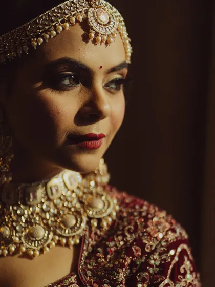 A close-up portrait with dramatic, moody lighting. The focus is on the bride's expressive eyes and the classic red lip, creating a look of timeless beauty.
