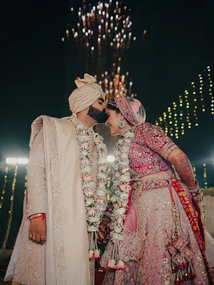 A spectacular moment of celebration. The groom kisses his bride's forehead as fireworks light up the night sky behind them.