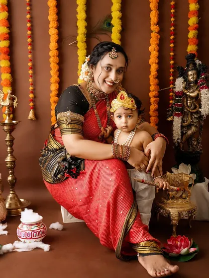A beautiful portrait of a mother and her baby Krishna, both adorned in traditional attire and jewelry, in front of a festive backdrop.
