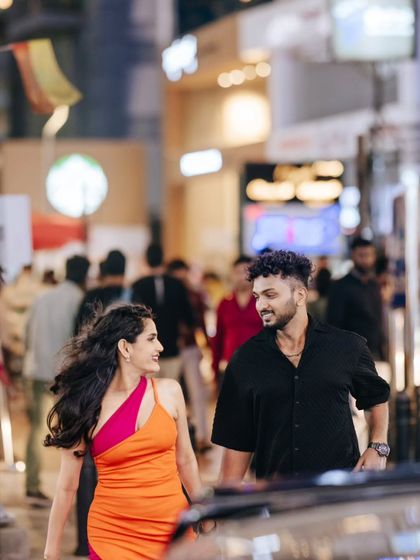 A candid shot of a couple walking through a busy, illuminated city market at night, capturing a natural interaction amidst the urban hustle.